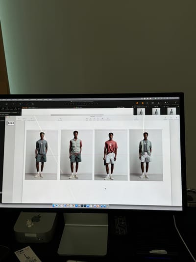 This media file shows a computer screen displaying a digital design or photo editing software. The main subject on the screen is a series of four images of a young Black man posing. He is dressed in casual, modern clothing, including shorts and t-shirts or light jackets in muted colors. The setting for these photographs appears to be a studio with a plain white background and subtle grid lines, suggesting a professional photoshoot for fashion or e-commerce.
On the left side of the screen, there are toolbars and menus typical of design software, with labels in Spanish such as "Edición," "Archivo," "Disposición," "Visualización," "Reproducir," and "Ayuda." The date "Mar 30 jun 15:45" is visible, indicating the time the file was accessed or modified. Below the images, there are file names like "2026_06_30_SPORT_GEORGE.cosessiondb" and "5-A6287.CR3," which are likely project or image identifiers.
To the right of the computer screen, several objects are visible on a dark surface. These include a compact Apple Mac Mini computer with an Apple logo, and other electronic devices or accessories. A small white figurine, possibly a cat or dog, is attached to the Mac Mini. A package with European Union (EU) markings and barcode is also present, suggesting it is an item that has been delivered or is being shipped.
The overall scene depicts a work environment, likely a creative professional's workspace, where digital media is being managed or edited. The image's lighting suggests it was taken indoors, possibly in the late afternoon given the timestamp. There are no explicit emotional cues from the subject in the photos, as they are presented in a neutral, professional manner. There are no obvious location cues to specifically link it to Fibracolor, Spain, beyond the potential context provided.