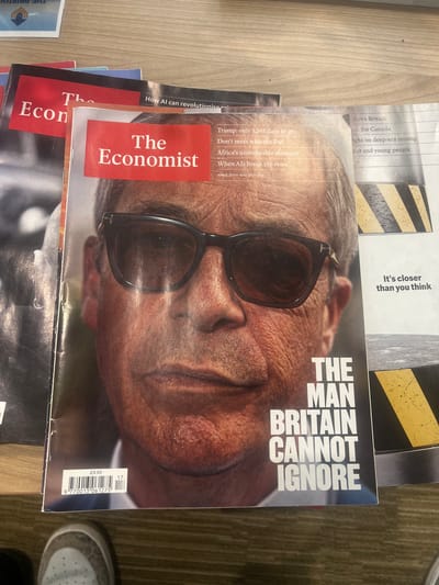 The image shows a stack of Economist magazines. The top copy features a cover image of a man with sunglasses. The cover text reads "THE MAN BRITAIN CANNOT IGNORE". Other text on the cover includes issue details for April 26th-May 2nd 2025 and article titles: "Trump: only 1,361 days to go", "Don't mess with the Fed", "Africa's unstoppable diaspora", and "When AIs break the rules". The price is listed as £9.99. Additional magazines are partially visible in the stack, including one with an article about AI. A section of another magazine mentions "shadows Britain", "lan for Canada", "fight on deep-sea mining" and "cancer and young people". A shoe is slightly visible at the right edge of the frame. The background appears to be a carpeted floor.