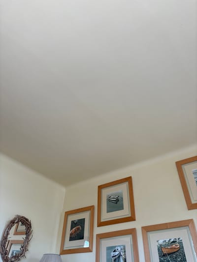 The image shows a corner of a room with white walls and a white ceiling. There are four framed pictures hanging on the wall. The pictures are all landscape-oriented and show boats in various settings. The pictures are all in simple wooden frames. The picture on the far right has a dark brown wooden frame. The image is shot from a low angle. The room appears to be in a private residence in Dinard, France, based on the provided coordinates.  The coordinates indicate a location in the town, near the coast.  It is impossible to determine the specific address or the identity of the owner of the residence.