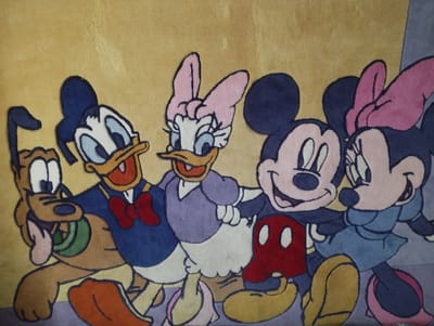 This is a close-up, eye-level shot of a rug featuring cartoon characters from Disney. From left to right, the characters depicted are Pluto, Donald Duck, Daisy Duck, Mickey Mouse, and Minnie Mouse. They are all smiling and appear to be standing closely together, possibly in a celebratory or friendly pose. The rug has a textured surface, and the characters are rendered with thick, dark outlines and flat, colorful fills. The background of the rug is a muted yellow. There is no indication of the city of Hnivan, Ukraine, or any urban environment within this image. The focus is solely on the rug and its design.