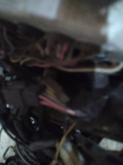This is a very blurry, dark, and close-up photograph of what appears to be electrical wiring. The image is heavily pixelated and lacks clear detail, making it difficult to definitively identify specific objects or a broader scene. There are several bundles of wires visible, with some appearing to be red, pink, yellow, and white. Some wires are thicker than others, and some have insulation that looks frayed or damaged. There are also some dark, amorphous shapes in the background that could be part of a larger electrical component or machine. The lighting is poor, with some areas of bright light and others in deep shadow, which further obscures the details. There is no discernible text or any indication of people, animals, or specific location cues within the image itself. The overall impression is one of a messy and complex electrical connection, possibly within a vehicle or an industrial setting, though this is speculative due to the lack of clarity. Given the location context of Gampongbaro, Indonesia, it could be related to local infrastructure or a household electrical system, but again, this cannot be confirmed from the image alone.