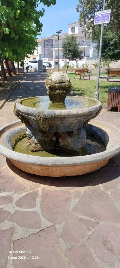 The image shows a stone fountain in a park in the city of Canals, Spain. The fountain is made of weathered stone and has multiple tiers with water collecting in the basins. The surrounding area is paved with flagstones. A sign indicating the "AJUNTAMENT DE CANALS" is visible in the background, and the text on the sign reads "SI ES TEU, ARREPLEGA EL QUE ES SEU." The image was taken on June 1, 2026, at 12:26 p.m., as indicated by the date and timestamp in the lower right corner. The camera used was a Galaxy M52 5G.