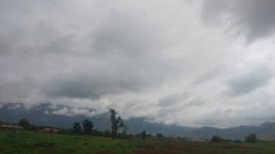 The image shows a landscape scene with a prominent sky filled with clouds. In the upper portion of the image, a dark, hilly landscape is visible, with some greenery and hints of structures or buildings. The sky is overcast, with various shades of gray and white clouds suggesting either an impending storm or a generally cloudy day. The overall impression is of a natural, possibly rural setting. The image is oriented such that the landscape appears at the top and the sky dominates the bottom half. Due to the lighting and cloud cover, it is difficult to determine the exact time of day, but the atmosphere suggests it could be morning or afternoon. There is no visible text in the image. The location context provided is Gidan Waya, Nigeria, which would imply a tropical or subtropical environment, consistent with the lush greenery and cloudy sky.