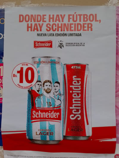 This is a close-up shot of an advertisement for Schneider beer, likely located in Municipio Tarija, Bolivia. The poster is predominantly white with red lettering and features two cans of Schneider beer. The left can is adorned with the Argentinian flag's blue and white stripes and images of soccer players, most notably Lionel Messi. A red circle with the text "Bs. 10" indicating the price, is prominently displayed. The right can is red with white lettering. Text at the top reads "DONDE HAY FÚTBOL, HAY SCHNEIDER" ("Where there is soccer, there is Schneider"). The advertisement states that this is a "NUEVA LATA EDICIÓN LIMITADA" ("New Limited Edition Can"). Additional text states that Schneider is the "SPONSOR OFICIAL DE LA SELECCIÓN ARGENTINA" ("Official Sponsor of the Argentinian Selection"). The bottom of the poster has a warning about excessive alcohol consumption and prohibits sales to minors. The overall impression is of a promotional poster for Schneider beer leveraging the popularity of soccer and the Argentinian national team.