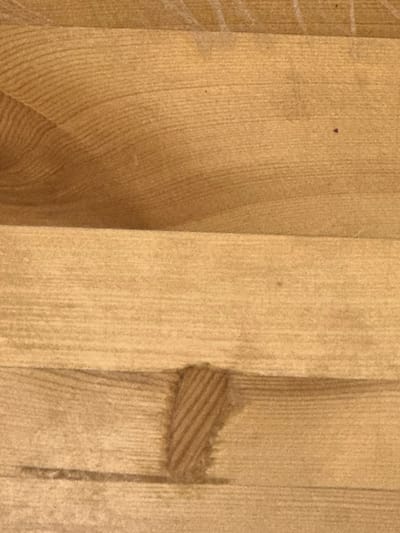 This is a close-up, overhead photograph of a light brown wooden surface. The wood has a visible grain pattern running horizontally across the image, with subtle variations in color and texture. There are faint white lines visible on the upper portion of the surface, possibly from previous markings or wear. In the lower middle section, there is a darker, textured patch that appears to be a knot or a flaw in the wood. The lighting suggests an indoor environment with diffuse illumination, highlighting the natural characteristics of the wood. The image does not provide any contextual information that would allow for its placement within Letterkenny, Ireland, or any specific city.