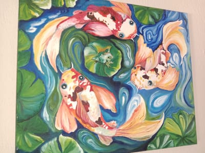 This is an oil painting of three koi fish swimming in a pond surrounded by lily pads. The fish are primarily orange, white, and black, with large blue eyes. A small green frog sits on a lily pad in the center of the pond. The water is depicted with swirling brushstrokes of blue and white, and the lily pads are a vibrant green. The painting is hung on a white textured wall, and the lighting suggests it is indoors. There is no information about the location in Bayraklı, Turkey.