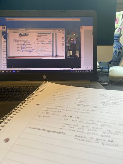 A person is participating in a virtual meeting on a laptop, possibly a class or seminar, based on the visible content on the screen. The meeting involves multiple participants. The laptop is placed on a desk with a notebook. The notebook contains handwritten notes in German. The laptop screen displays a PowerPoint presentation in German, which appears to be related to German grammar and vocabulary. The meeting is being conducted through an online platform. The name of the meeting host/institution is "Centro Universitario de Idi," and the date displayed on the taskbar is 2/5/2026. No specific information about the location in Villaviciosa, Spain, is provided.