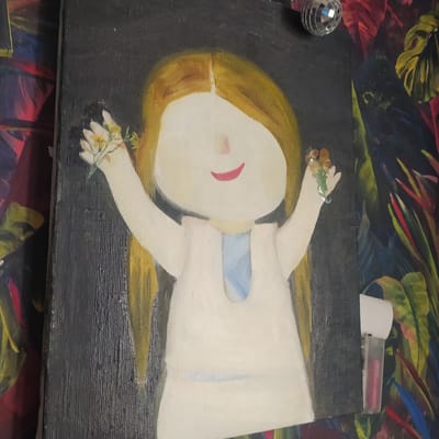 The image shows a painting of a child with blonde hair and a blank face, wearing a white dress. The child is holding small bouquets of flowers in each hand. The painting is on a canvas with a dark background. The painting is hanging on a wall, and to the right of the painting, there is a section of wallpaper with a colorful floral pattern. A small, silver disco ball is visible hanging from the ceiling in the upper right corner of the image. A white object with a pink tube inside is attached to the wall on the right side of the painting, obscuring a portion of the floral wallpaper. There is no indication or information suggesting this image is located in the city of Bucha, Ukraine.