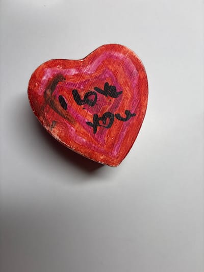 The image shows a heart-shaped object with the words "I love you" written on it in black marker. The object is red and pink, with visible wood grain. It is lying on a white surface. The image does not provide any information about the location in Velbert, Germany.