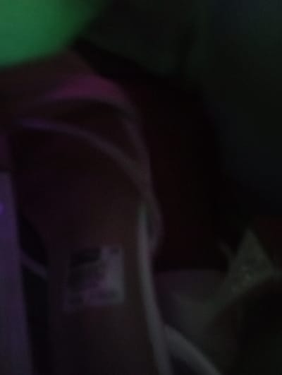 The blurry image presents a dark and indistinct scene. Dominant colors are dark brown, green, and purple. White cables or wires are vaguely visible. There's a small, rectangular patch of color with indistinguishable details possibly a sticker or label. Light sources are dim and uneven, contributing to the unclear and mysterious nature of the composition.