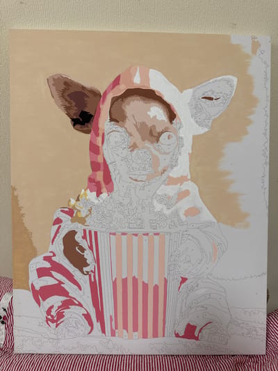 The image shows a partially completed paint-by-numbers canvas depicting a chihuahua wearing a hooded blanket and holding a bucket of popcorn. The chihuahua's face is detailed, with visible numbers for painting. The bucket has pink and beige stripes, and some popcorn pieces are visible. The background is a solid beige color. The canvas is positioned on a surface covered with a red and white striped fabric. The image does not contain information related to Nikolina Gora, Russia.