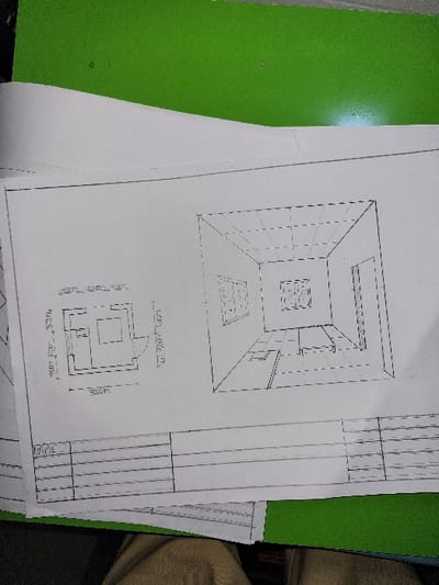 The scene displays a sheet of white paper containing two architectural or engineering drawings, resting on a bright green surface. The upper left portion of the paper is slightly curled. On the left side of the paper, a top-down floor plan is depicted, labeled "DORMITORIO" (bedroom). This plan shows a rectangular room with a square object positioned centrally, likely representing a bed or furniture, and an opening on the right side, indicating a doorway. A dimension of "3000m" is annotated horizontally at the bottom of this plan, likely a typographical error for 3.00m or 3000mm. To the right, a perspective drawing illustrates the interior of a room, featuring walls with recesses or openings, a gridded ceiling, and a central square feature on the floor. Below these drawings, a blank title block or table with multiple rows is present at the bottom of the paper. The paper itself is slightly wrinkled. The green surface beneath appears to be a desk mat, folder, or another document. A portion of a light brown, possibly fabric, object is visible at the very bottom edge of the frame, suggesting the presence of a person or a personal item interacting with the documents. No visual information within the image identifies a specific location in the city of Puerto López, Colombia.
