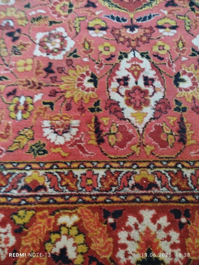 The image shows a close-up view of a richly patterned rug with a dominant red background. Intricate floral motifs are visible in shades of red, yellow, white, and black. A decorative border runs across the middle of the image, featuring geometric patterns in similar colors. The bottom section of the rug displays more of the floral design. Text overlays at the bottom left read "REDMI NOTE 13", and at the bottom right, "19.06.2026 18:38". The overall impression is of a decorative textile. This image does not provide any information about the city of Yangibazar, Uzbekistan, or any specific location within it.