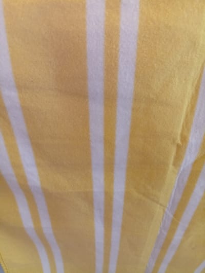 This is a close-up, abstract image of a yellow and white striped fabric. The stripes are vertical and evenly spaced, with the yellow being the dominant color. The fabric appears to be soft and textured, possibly a blanket or a piece of clothing. There are no people, objects, or scenes visible, nor any activity or event taking place. The lighting is even, and there are no strong shadows, suggesting it was taken in good, diffused light. There are no discernible location cues, text, or emotions conveyed in the image. The crops provided focus on different sections of the fabric, highlighting the texture and pattern.