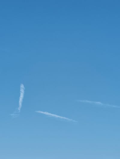 The image displays a clear blue sky with two wispy clouds. One cloud is positioned in the upper left quadrant, appearing as a vertical streak. The second cloud is located in the lower right quadrant, stretched horizontally across the frame. No people, objects, or identifiable structures from Georgsmarienhütte, Germany are visible in this image. The scene is entirely dominated by the sky and the faint cloud formations.
