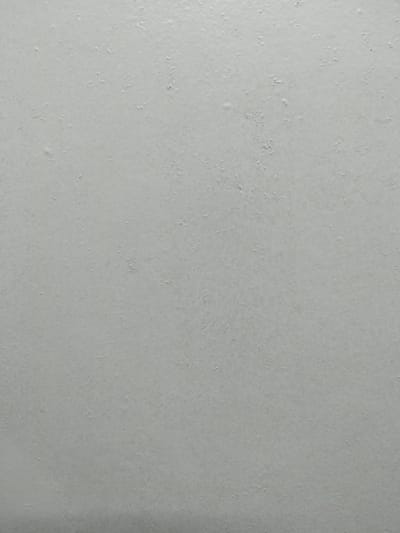 The image is a close-up, full-frame shot of a light gray, textured surface. The texture appears to be consistent with a painted wall that has minor imperfections, such as small chips, bumps, and slight variations in the paint application. There are no discernible objects, people, or actions in the image. The lighting is even and diffuse, creating no strong shadows and allowing the subtle texture of the surface to be visible. The location in Гожскі сельскі Савет, Belarus, cannot be determined from the visual information provided in the image alone.