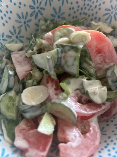 The image is a close-up, overhead shot of a salad in a bowl with a blue and white floral pattern on its rim. The salad appears to be made with chopped tomatoes, cucumbers, and possibly green onions, all coated in a creamy dressing. The lighting is bright, suggesting it was taken indoors during the day. There are no people or specific landmarks visible in the image that would allow for a precise location within Richmond Hill, Canada.