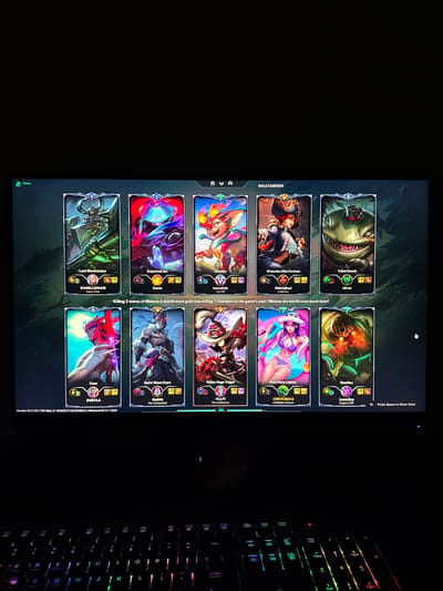 The image shows a computer screen displaying the champion selection screen of the game League of Legends. The screen displays several champion portraits with their names and summoner names. The screen also shows a message that "Killing 3 waves of Minions is worth more gold than killing 1 champion at the game's start. Minions are worth even more later!" The screen also shows the version number of the game. A keyboard is visible to the right of the screen. The image does not contain any information that would suggest the location of the photo is in Bratya Daskalovi, Bulgaria.