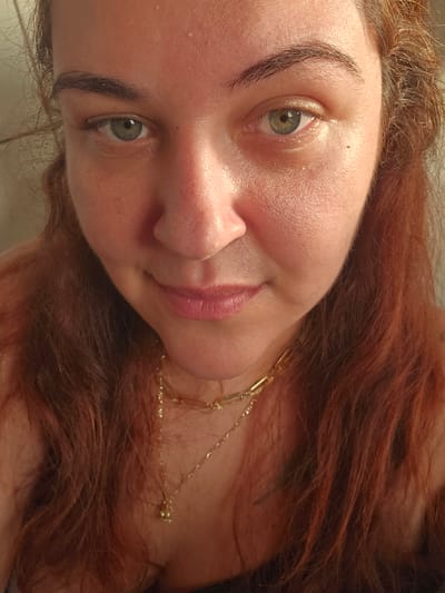 A close-up portrait of a woman with red hair, light skin, and green eyes, wearing a gold necklace. The photograph is taken at an angle, with the woman's face tilted towards the camera. There is no verifiable information in the image to indicate a location in Zirndorf, Germany.