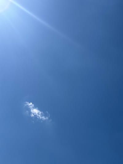 This is a vertical, full-frame, eye-level, medium shot of a bright blue sky with a single small, fluffy white cloud positioned in the lower left quadrant of the frame. A bright sunbeam enters from the upper left corner, casting a diagonal line of light across the sky. The location is Драчкаўскі сельскі Савет, Belarus, but the image is entirely natural, showing only sky and sunlight, with no man-made structures or human presence visible.