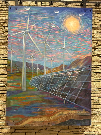 The image displays a painting mounted on a stone wall. The painting depicts a landscape with wind turbines and solar panels, suggesting a focus on renewable energy. The sky is painted with swirling strokes of orange, pink, and blue, with a bright yellow orb representing the sun. Several wind turbines are visible in the middle ground, with what appear to be oil pump jacks in the distance. In the foreground, a large array of solar panels is depicted at an angle. The overall style of the painting is impressionistic, with visible brushstrokes and vibrant colors. The location is identified as Unknown, United States of America.
