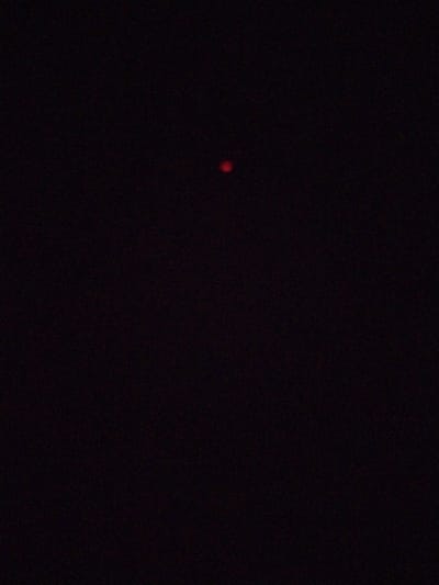 The image is a close-up, low-light photograph of a small, reddish-pink, out-of-focus dot against a completely black background. The dot appears to be a point of light, possibly a distant light source, reflection, or a small illuminated object. The background is uniformly dark, with no discernible features, textures, or environmental context. The image's overall quality is grainy, suggesting it was taken in very low light conditions or with a low-quality camera. There is no indication of the city of Ștefan Vodă, Moldova, or any urban environment.