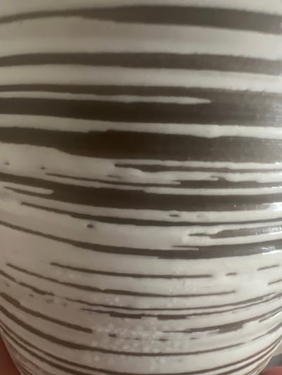The image displays a close-up view of a ceramic object with a striped pattern. The stripes are horizontal and vary in thickness, alternating between a dark brown or grey color and a white or cream color. Some of the white stripes have an uneven, textured appearance with small darker specks or irregularities. The lighting suggests a smooth, possibly glossy surface. No other objects, people, or environmental details are visible in the image. The location in West Hartford, United States of America, is not discernible from the visual content of the photograph.
