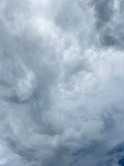 The image depicts a cloudy sky. The clouds are predominantly gray and white, suggesting an overcast or potentially stormy weather condition. There is no indication of the location being in Tlik, Armenia, or any other specific location. There are no people, subjects, objects, actions, or interactions visible in the image. The environment consists solely of clouds and a hint of blue sky peeking through in the upper right corner.