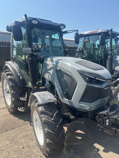 This image shows a close-up, rotated view of a FOTRAK LGF 904 tractor parked outdoors. The tractor is predominantly gray with black accents on the grille and various components. Key visible elements include the front grille, headlights, mirrors, tires, and parts of the cabin. The tractor appears to be new, with some plastic wrapping still visible on a part of the front. The setting is outdoors, with a clear blue sky suggesting daytime and fair weather. The ground is paved with asphalt. There are shadows visible on the ground, cast by the tractor and possibly other unseen objects, indicating the sun is at an angle. The text "FOTRAK" and "FOTRAK LGF 904" is visible on the tractor's body and tires. The context of Khryplyn, Ukraine, suggests this is likely a photograph taken in an agricultural or industrial setting within that region. There are no people visible in the image. The overall impression is that of a product display or a moment of showcasing the machinery.