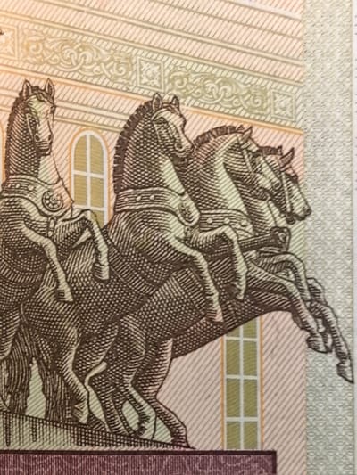 The image is a close-up of a postage stamp featuring an engraving of a chariot pulled by four horses. The horses are depicted in profile, with intricate details of their harnesses and the chariot's design visible. The background shows architectural elements, suggesting a classical or historical setting. The stamp's design is rendered in a monochromatic style, predominantly in shades of brown and beige, with some subtle color accents from the paper itself. There are no visible people in the image. The stamp appears to be part of a larger collection or series, given the intricate detailing and thematic subject matter. The location in Ново-Талицы, Russia is not discernible from the image itself.