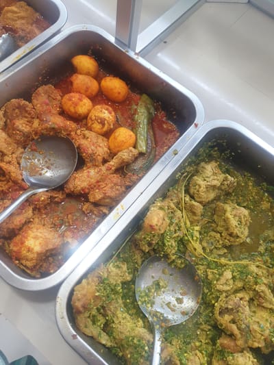 This is an overhead, close-up shot of three metal food pans in what appears to be a food court or buffet setting. The pans are filled with various Indonesian dishes. The pan on the left contains pieces of fried chicken and several hard-boiled eggs in a red, spicy sauce, garnished with chili flakes and green chilies. The middle pan holds a similar dish, with more chicken and eggs in a reddish sauce. The pan on the right is filled with pieces of chicken covered in a vibrant green, herbaceous sauce, possibly a spicy herb paste. Two serving spoons are visible in the pans, one in the left pan and another in the right. The background shows a light-colored tiled floor and the edge of a counter. The overall impression is of a colorful and appetizing display of local cuisine.