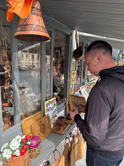 A man is looking at goods in a display case in the city of Arzamas, Russia. The case contains dolls, wooden dishes, and other items. The man is holding a wooden plate.