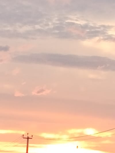 A serene sunset in Yashkino, Russia, paints the sky with hues of pink, orange, and lavender. Wispy clouds drift across the horizon, illuminated by the fading sunlight. In the foreground, a solitary utility pole stands tall, its silhouette stark against the vibrant sky. Power lines extend outwards, connecting to unseen structures. The scene is tranquil and devoid of human presence, capturing the quiet beauty of a rural evening.