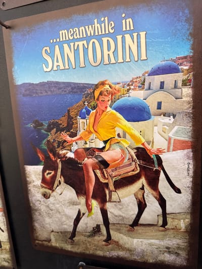 A vintage-style poster depicts a woman riding a donkey along a pathway in the town of Santorini, Ia Municipal Unit, Greece. The woman, dressed in a yellow shirt, short skirt, and thigh-high stockings with garters, is seated sideways on the donkey, facing left. She has blonde hair tied up with a yellow scarf and her gaze is directed towards the left. The donkey is brown with white markings around its eyes and muzzle. The background features the iconic white buildings with blue domes and a panoramic view of the Aegean Sea. The text "...meanwhile in SANTORINI" is prominently displayed at the top of the poster. A signature, "MATERNA C", is visible on the right side of the poster.