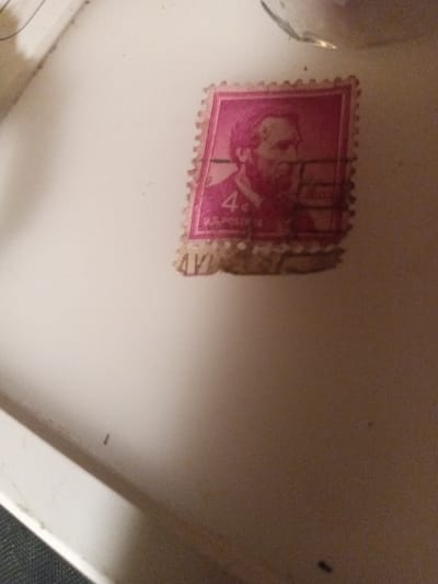 The image shows a worn, pink, US postage stamp with a portrait of a man with a beard and a "4c" denomination. It is lying on a white surface that appears to be a table or countertop. The image was taken in Kitchener, Canada (latitude: 43.428, longitude: -80.479).