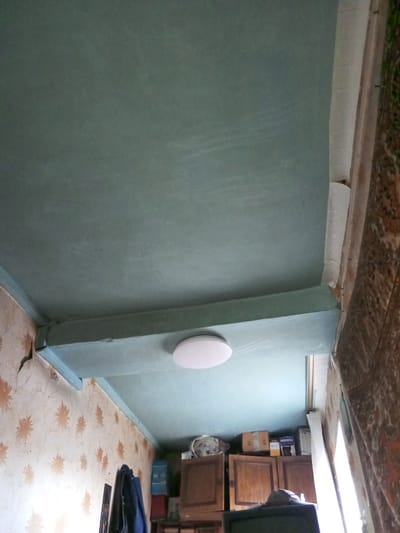 The image shows the interior of a room. The walls are covered in floral wallpaper. The ceiling has been painted a blue-green color. There is a ceiling light fixture in the middle of the room. There is a cabinet against the far wall and a curtain on the right. The image does not contain information to place this location specifically in Parabel, Russia.