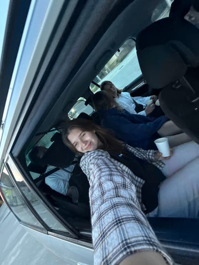 A group of four people are in a car. One person is holding a cup. The car is moving. The location is presumed to be Ruma Municipality, Serbia.