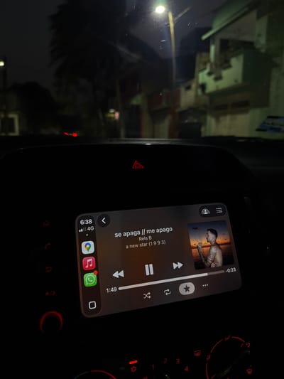 The photo shows a car's infotainment system at night. The screen displays the song "se apaga // me apago" by Rels B from the album "a new star (1993)". The song is partially played, with 1:49 elapsed and -0:23 remaining. The system is connected to a phone showing 6:38 AM, 4G connectivity, and notifications from apps like Google Maps, Apple Music, WhatsApp, and others. The hazard lights are illuminated. The car's interior is otherwise dark.