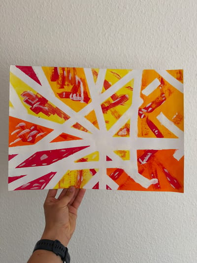 A hand with a black watch is holding up a painting against a white, textured wall. The painting is abstract, featuring bold white lines forming geometric shapes against a background of bright orange, yellow, and red brushstrokes. The brushstrokes appear energetic, with some areas showing thick, impasto application and others more diluted. The overall impression of the painting is vibrant and dynamic. The white lines are applied with a different texture, appearing flatter and smoother than the colorful background, suggesting a layering technique. The hand holding the painting is relaxed, with the fingers slightly curled around the edge, and the watch is visible on the wrist. The lighting is neutral, indicating an indoor setting, likely a room. There is no visible text in the image. The setting appears to be Nienburg/Weser, Germany.
