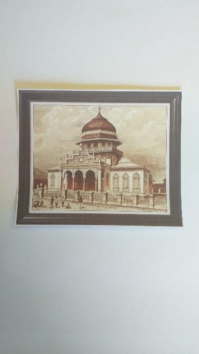 The image displays a physical sepia-toned print, bordered by a dark frame and a thin white inner margin, resting on a plain white, flat surface. The print depicts an elaborate, multi-tiered building, identified as a mosque, located in Limpok, Indonesia. The central structure of the mosque features a prominent, bulbous dome with a finial, surmounting an ornate, multi-level base that includes an octagonal section. The primary facade presents a series of three large, pointed arches forming a deep portico, supported by columns. The building's side wings contain several rectangular windows with decorative frames. A low, decorative fence runs along the immediate foreground of the mosque. Approximately seven to ten indistinct human figures are scattered on the paved ground area in front of the building, engaged in various actions such as standing, sitting, or milling about. The environment includes a partly cloudy sky above the mosque and a faint architectural structure visible in the distant background to the right. The illustration is rendered with primary brown and reddish-brown hues against a lighter, desaturated backdrop.
