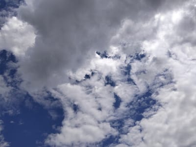 The image shows a view of the sky above Bulaev, Kazakhstan, filled with clouds against a deep blue background. The clouds are a mix of white, fluffy cumulus clouds and larger, darker gray formations that suggest they are thicker and possibly bring precipitation. Sunlight is visible, filtering through some of the thinner cloud layers, creating brighter patches and casting shadows within the cloud masses. The image is a close-up of the sky, with no ground features or human elements visible. The perspective is looking directly upwards.