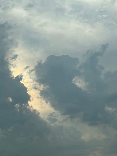 This media file captures a dramatic sky filled with clouds. The image is dominated by various shades of gray and white, indicating a cloudy day. The clouds are dense and textured, with some appearing fluffy and light, while others are dark and ominous. A bright, almost golden light is visible peeking through a gap in the clouds, creating a stark contrast and highlighting the dramatic formation of the cloudscape. This suggests either sunrise or sunset, or possibly a break in stormy weather. The orientation of the image appears to be rotated, with what would typically be the top of the sky now on the left. There are no visible people, objects, text, or specific location cues other than the provided context. The overall impression is one of natural beauty and the dynamic forces of weather.