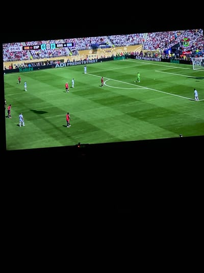 The image shows a broadcast of a soccer match on a television screen. The score displayed is 0-0 between ESP (Spain) and ARG (Argentina), with the time at 01:45. The stadium is filled with spectators, and advertising banners are visible along the perimeter of the field. The scene depicts a professional soccer game in progress. The location is not specified within the city of Legenda, Egypt; the image depicts a soccer match broadcast on a screen.