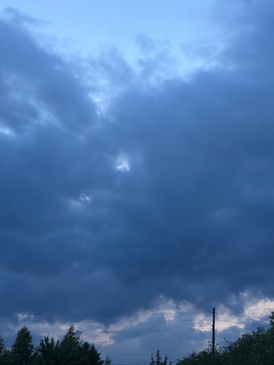 The media file depicts a cloudy sky, viewed from below. The sky is predominantly filled with dark, heavy clouds, suggesting an overcast or impending storm. To the right of the image, a utility pole with power lines stretches vertically, intersecting the cloud cover. Beyond the power lines, a dense canopy of green trees forms a border along the right edge.

The overall impression is one of a somber or dramatic atmosphere, likely due to the dark clouds. The time of day is difficult to ascertain precisely, but the lighting suggests it could be late afternoon or early evening, or a time when the sun is obscured by thick clouds. The presence of trees and utility poles indicates an outdoor, potentially rural or suburban setting, consistent with the provided location context of Petukhi, Russia. No people or specific activities are visible. The image is devoid of any discernible text.