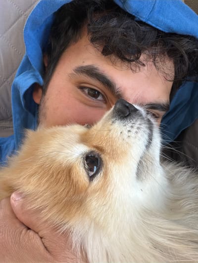 A close-up, tilted shot shows a person and a dog. The person, likely male, has dark hair and brown eyes, and is wearing a blue hoodie. The dog, a fluffy light-brown and white breed, is close to the person's face. The person is holding the dog. The location, Cuautla, Mexico, is not directly discernible from the image alone.