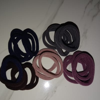 The image shows five piles of hair ties on a white, marble-patterned surface. The piles are arranged in a row, with dark blue, brown, gray, pink, and purple hair ties. The location is not specified and there is no indication or information of it being in Jatisari, Indonesia.
