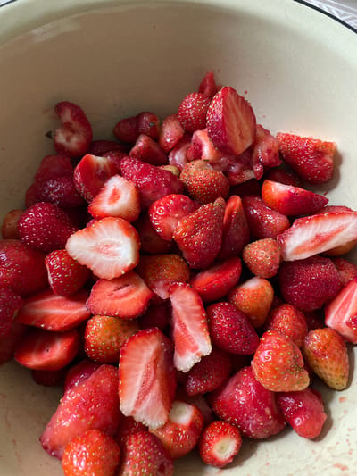 A close-up, overhead shot shows a bowl filled with sliced strawberries. The strawberries are a vibrant red, with some showing their white, seedy interiors. The bowl itself is a pale yellow, with a light brown rim. The lighting is natural, casting soft shadows. There are no people or other objects visible in the image. The scene is devoid of any identifying details that would place it in Izborsk, Russia, or any other specific location.