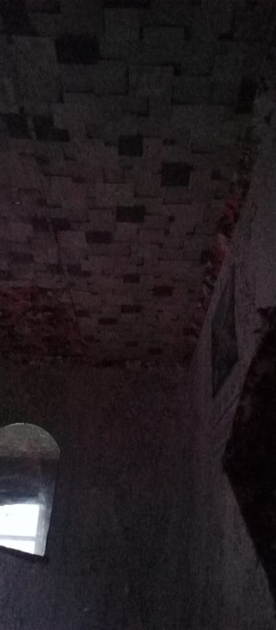 The image depicts an interior scene, likely in a dimly lit, possibly abandoned or old building. The ceiling appears to be constructed of rectangular blocks, laid out in a repeating pattern, with some areas showing exposed red brickwork, suggesting age and potential disrepair. To the left of the frame, a window with a curved top is visible. Light is emanating from outside the window, illuminating a portion of the interior wall. The rest of the environment is dark and indistinct, with shadows obscuring details of the room and any potential inhabitants or objects. The location of Marinovka, Kazakhstan, is a specific geographical context for this scene.