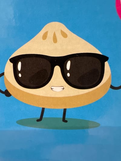 The image is a close-up, low-angle, vertical shot of a cartoon character, likely a dog, against a solid blue background. The character appears to be wearing large, dark sunglasses, which cover a significant portion of its face. The sunglasses have a thick black frame, and the lenses are solid black with two small white oval highlights within each lens, suggesting a glossy or reflective surface.

The character's face is a light tan color, with two small, dark tan spots on its snout. A small, white mouth with a faint outline is visible below the sunglasses. The character has a round, tan-colored head that extends off-frame to the right, with a darker tan band around the top. A black, curved line, possibly a tail or ear, extends upwards from the top of the head, also off-frame.

To the right of the character, a tall, elongated, teal-green shape is visible, resembling a surfboard or a large leaf. Two thin, black lines extend from the character's head area towards this teal shape, appearing to be legs or supports. One leg is bent, with a hook-like end.

A sliver of a bright pink object is visible in the upper left corner of the image, also off-frame. The overall style is simple and graphic, with bold lines and flat colors. The image does not contain any visible text. The setting is abstract, with no discernible environmental cues to indicate a specific time of day, weather, or location beyond the provided context of Keila, Estonia. The overall emotion conveyed by the character, due to the sunglasses and stylized features, is one of coolness or indifference.