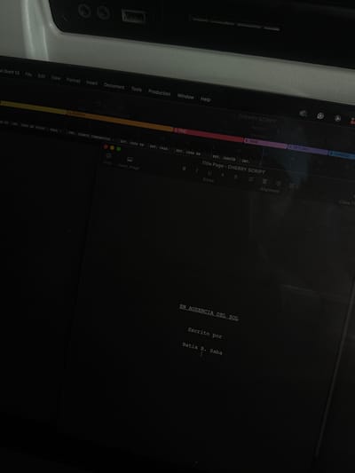 The image displays a close-up, angled view of a laptop screen operating in a dim, indoor environment. The screen is open to the Final Draft 13 scriptwriting application, which shows the title page of a document titled "CHERRY SCRIPT." The central text on the dark interface reads "EN AUSENCIA DEL SOL" (In Absence of the Sun), followed by "Escrito por" (Written by), and the name "Batua B. Saba." Above the script content, the application's menu bar is visible with standard options like File, Edit, View, Format, and Help. Below the menu bar, a horizontal timeline or scene breakdown is displayed, segmented with labels such as "4 SEARCH," "5 FIND," "6 TAKE," "7 RETURN," and "8 CHANGE." Further down, specific scene headings like "EXT. CASA EN VALLE - SALA," "INT. CUARTO COMPARTIDO," "EXT. CASA EN," and "EXT. JARDÍN" are discernible. Above the laptop, a light-colored, possibly textured surface is visible, featuring a dark USB port and other recessed slots. No individuals are visible in the frame. The scene is situated indoors in Hallandale Beach, United States.